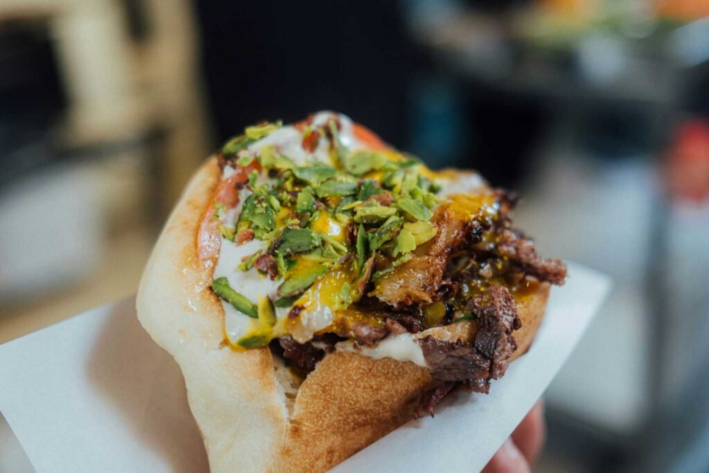 Doner kebab a closeup of kebab sandwich, featuring meat, sauce, and topping like pistachios, served in a bun.